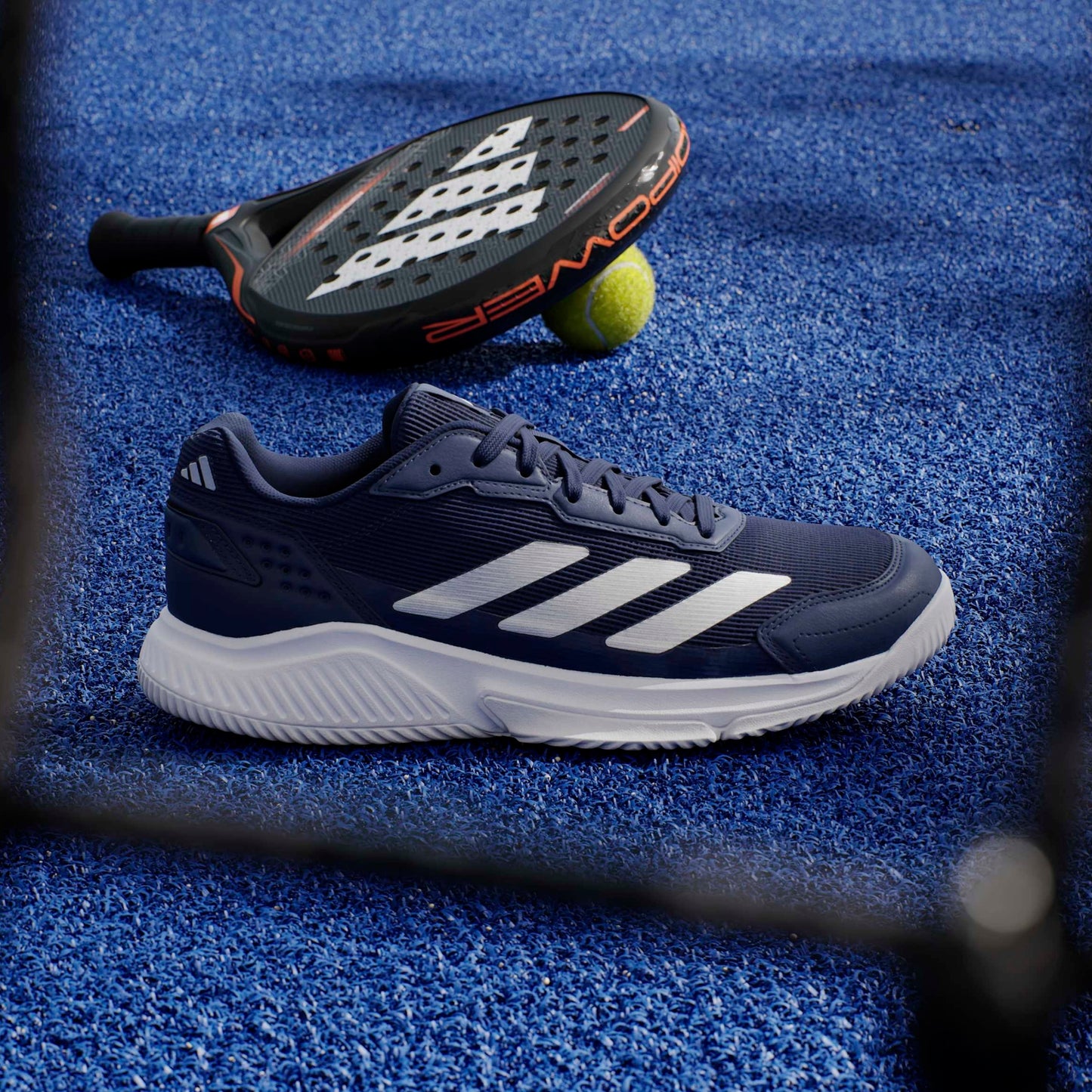 Navs adidas padel shoe on a blue court with a padel in the background