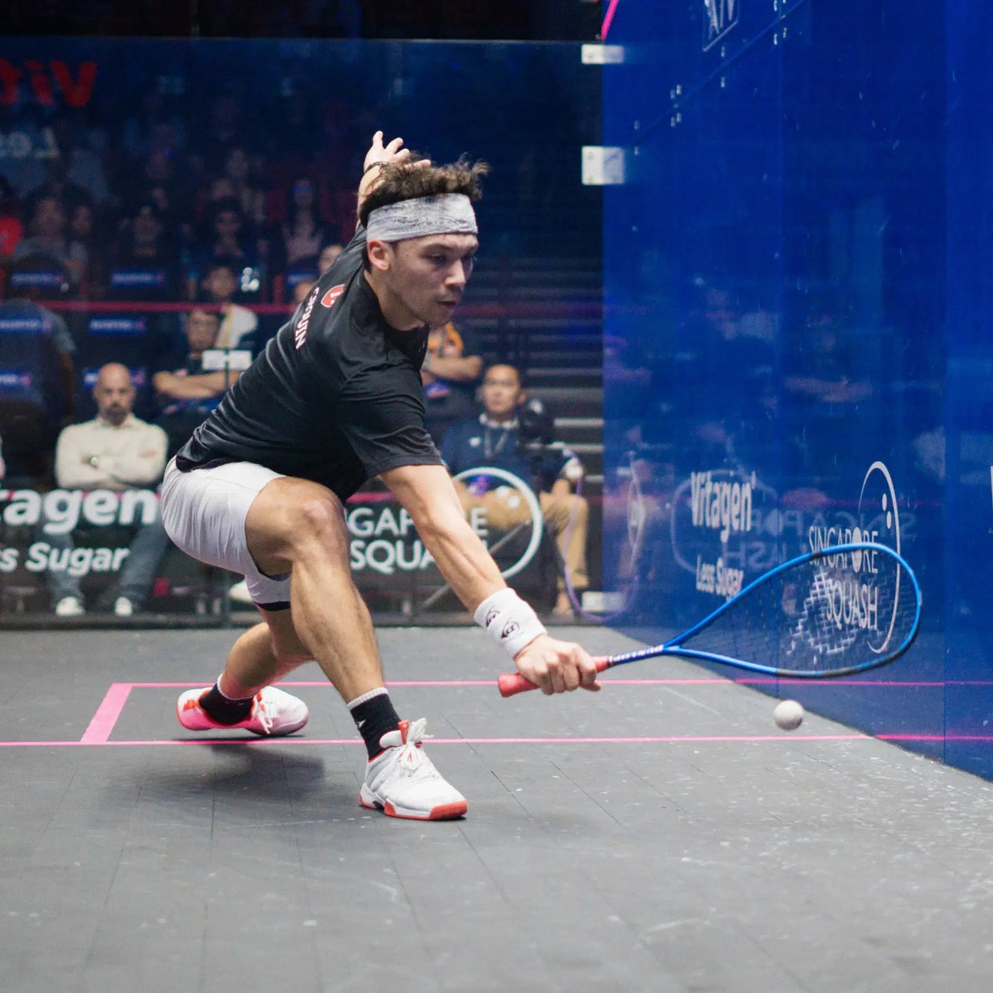 Squash player in action on a squash court with spectators in the background
