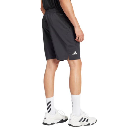 Person wearing black Adidas shorts and white sneakers on a white background