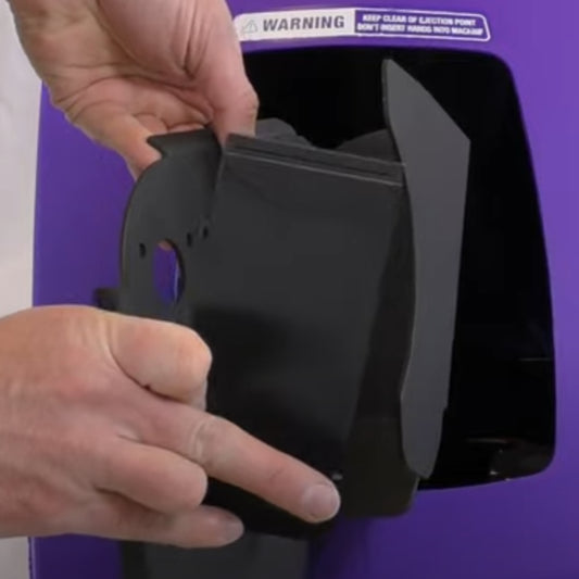 Person using a black tool on a purple surface with a warning label.