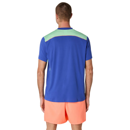 Man wearing a blue and green sports shirt with orange shorts on a white background