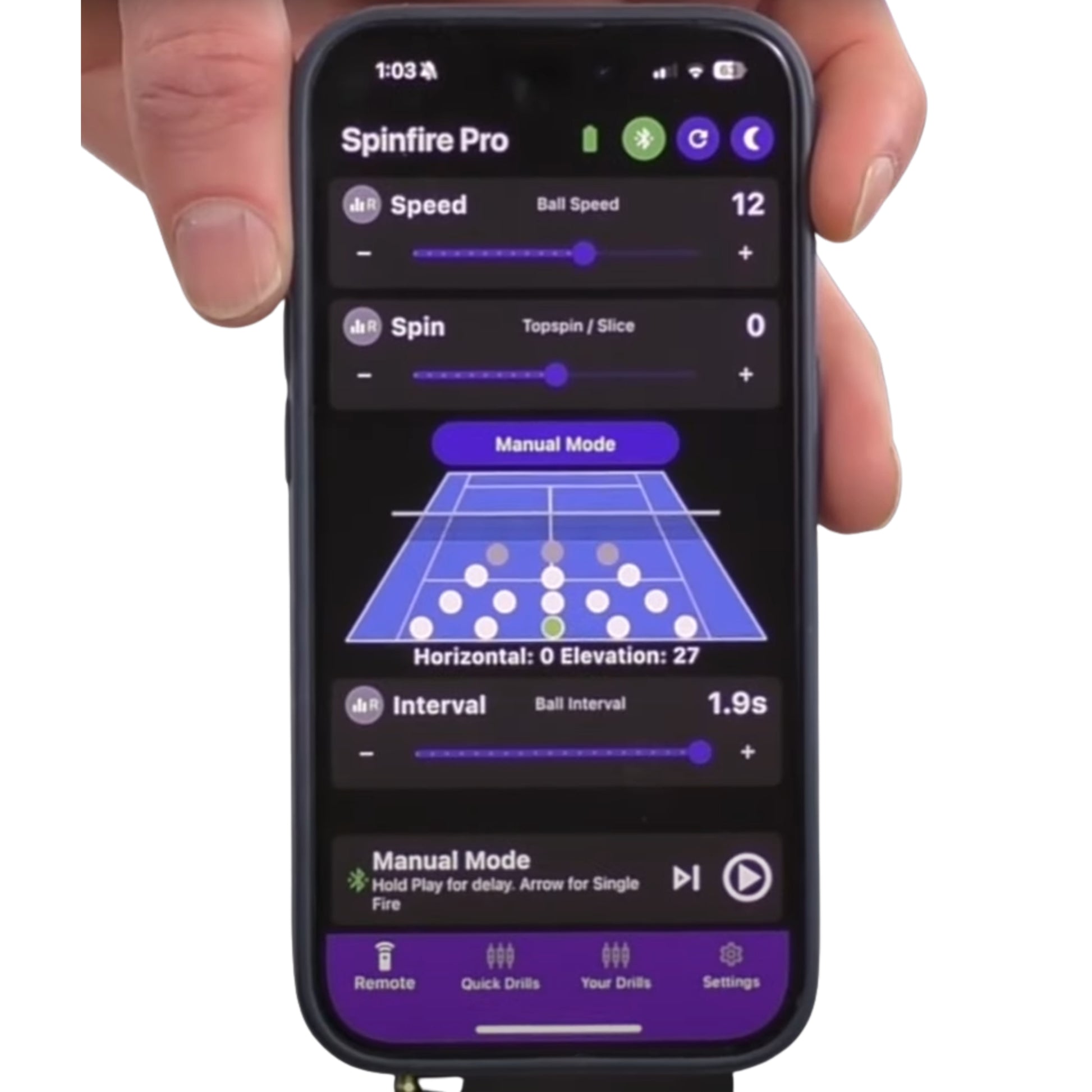 Phone displaying Spinfire Pro app with tennis court interface held by a hand