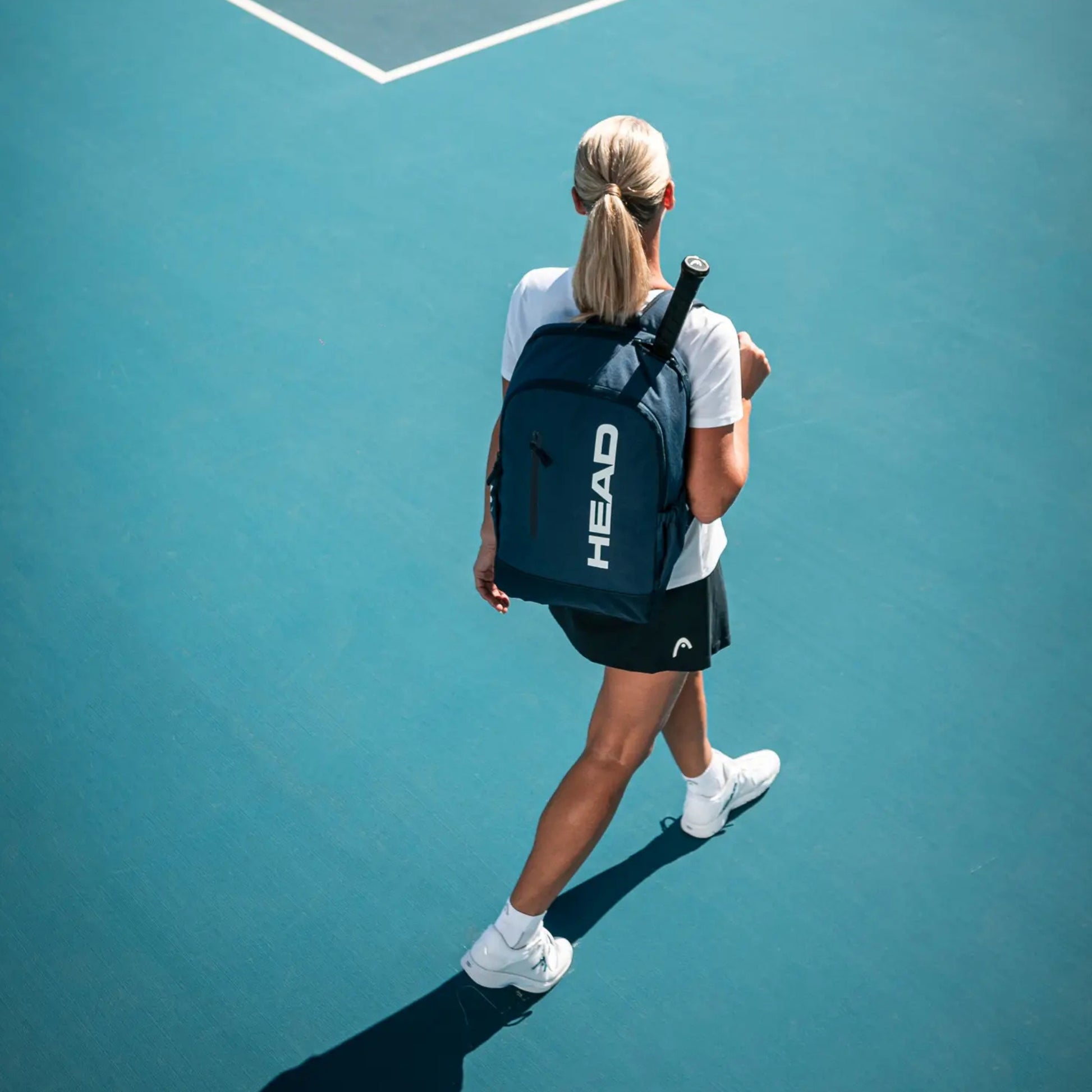 Person walking on a tennis court with a HEAD backpack