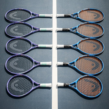 Eight Head tennis rackets arranged in two vertical rows on a blue tennis court, separated by a white center line. The rackets have purple, blue, and black frames with white and green grip tape, and brown stringing.