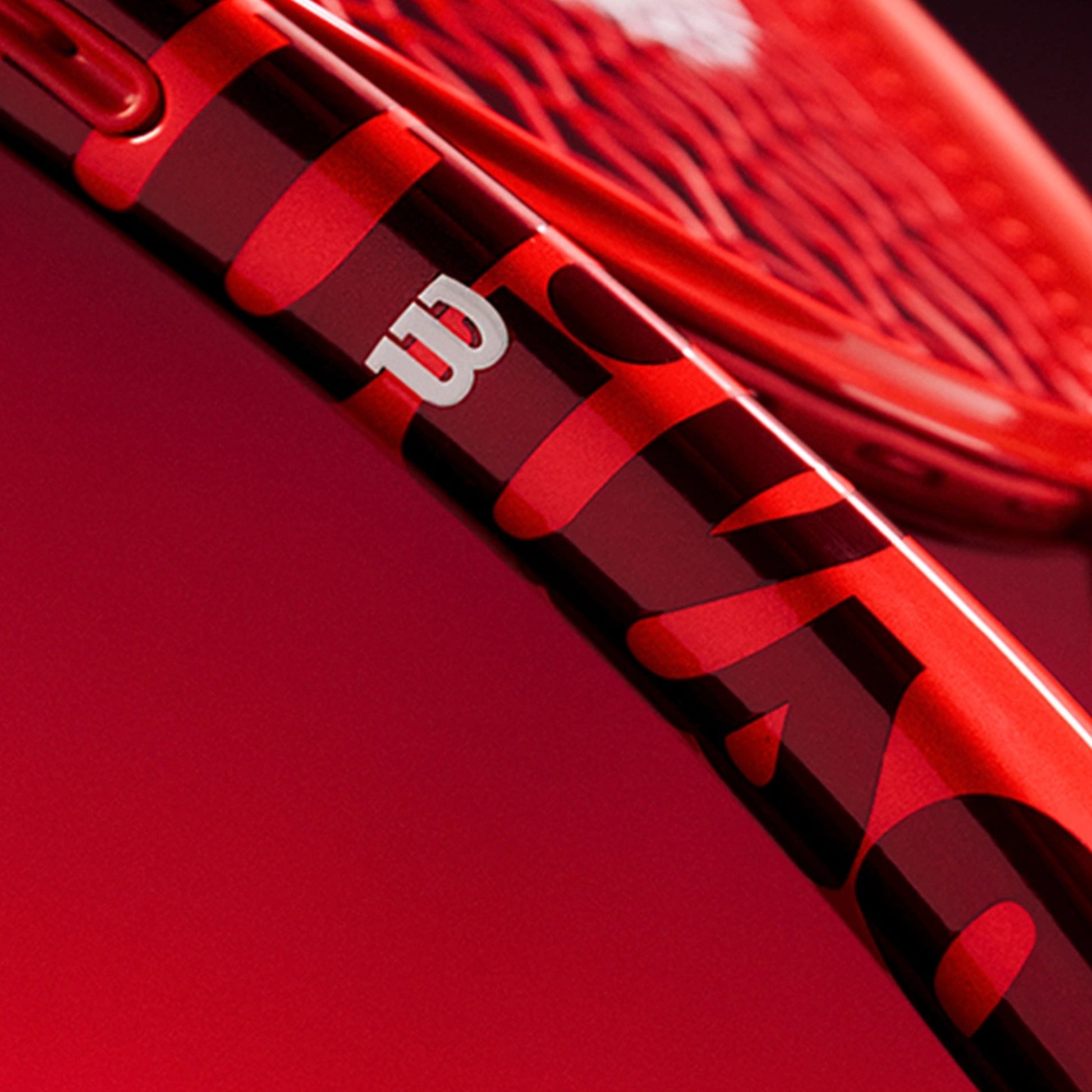 Close-up of a red and black Wilson tennis racket frame with a white Wilson logo, set against a matching red background.