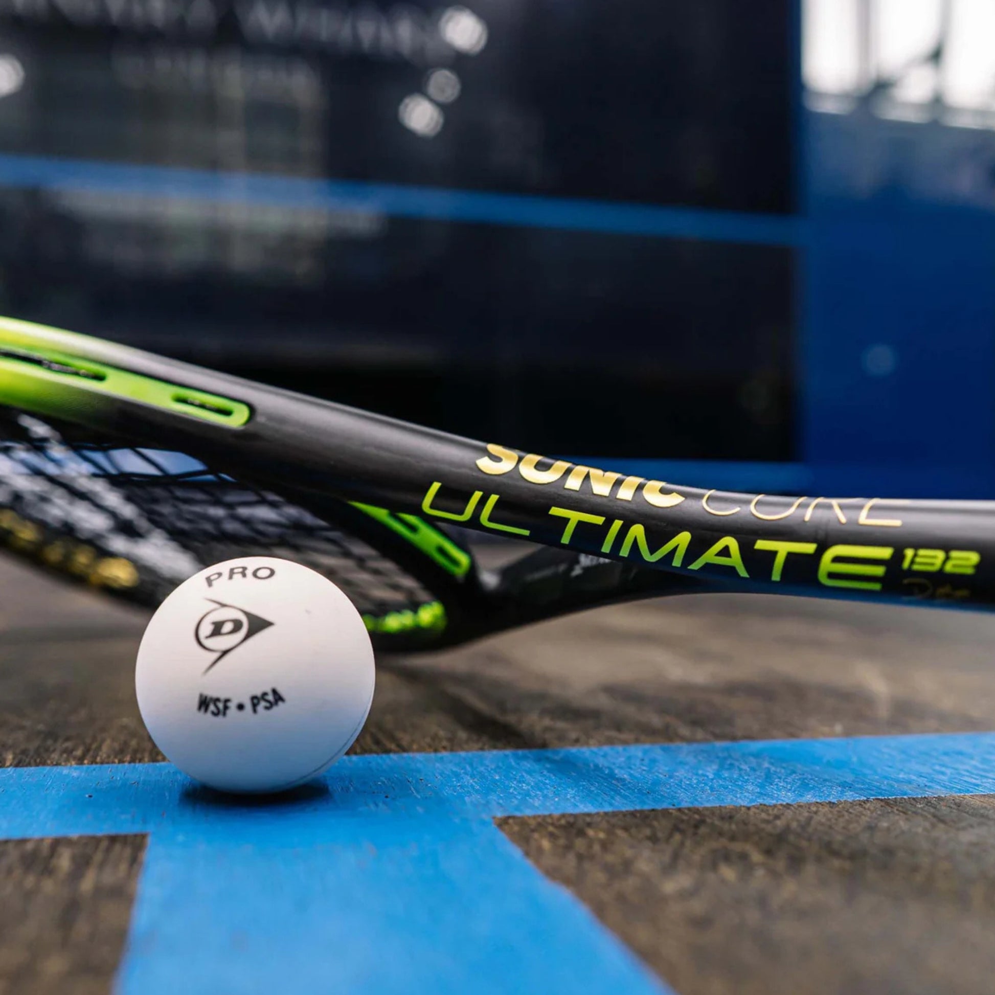 Black and yellow Dunlop squash racket lying on it's side on a court, with wording sonic core ultimate 132 on the side