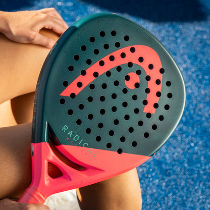 Person holding a green and red paddle with 'Radical' branding on a blue surface