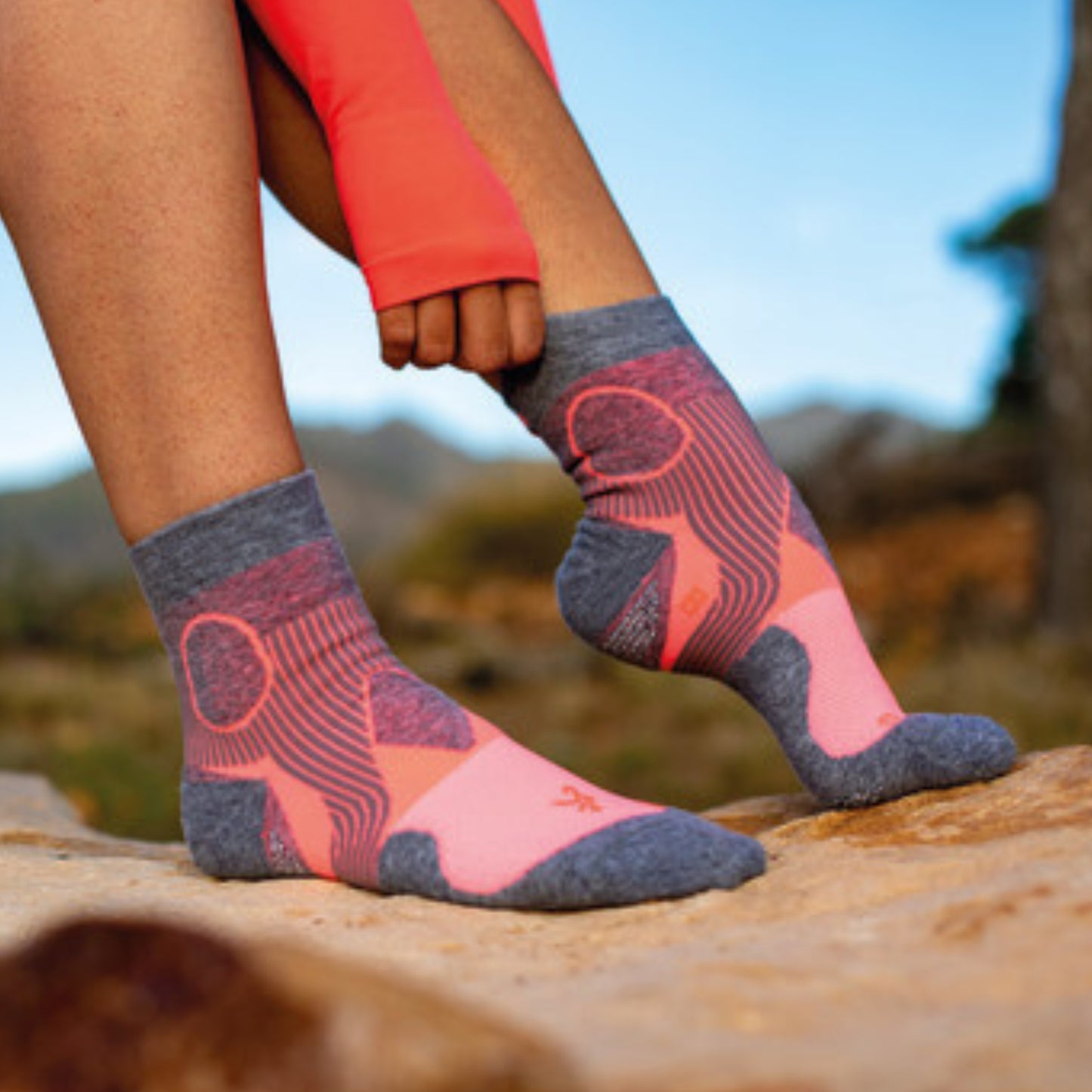 Person wearing pink and gray patterned socks outdoors on a rock