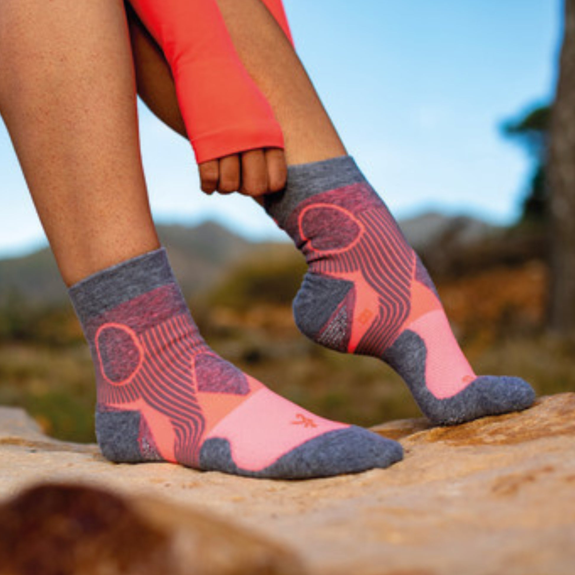 Person wearing pink and gray patterned socks outdoors on a rock