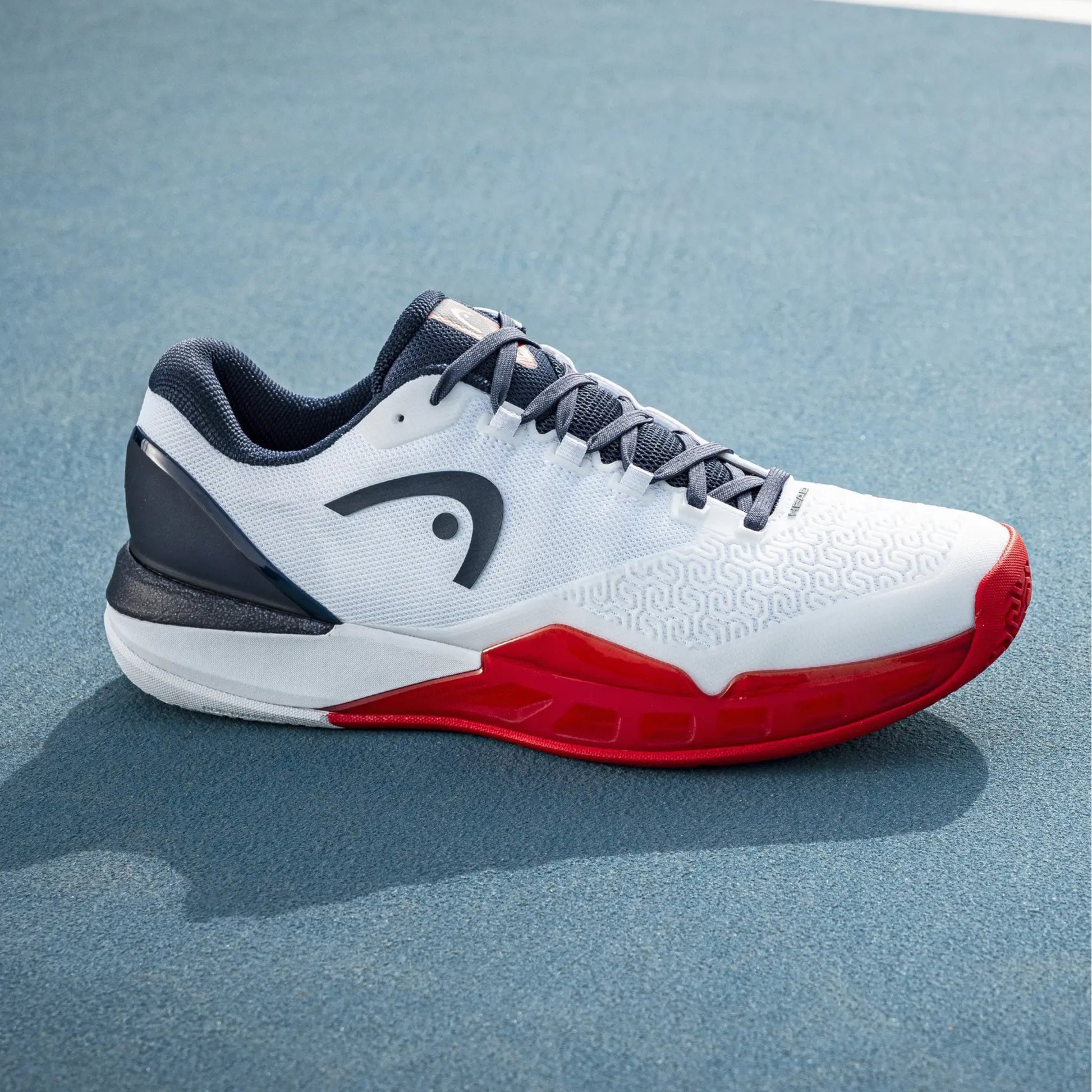 White Head tennis shoe with red sole on a blue court