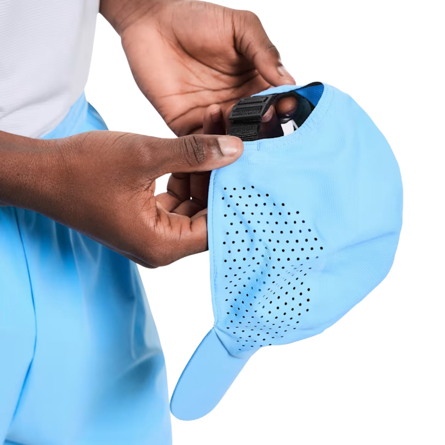 A close-up of a person's hands holding a light blue athletic cap with a side pocket, showing a black strap or accessory inside the pocket, against a white background.