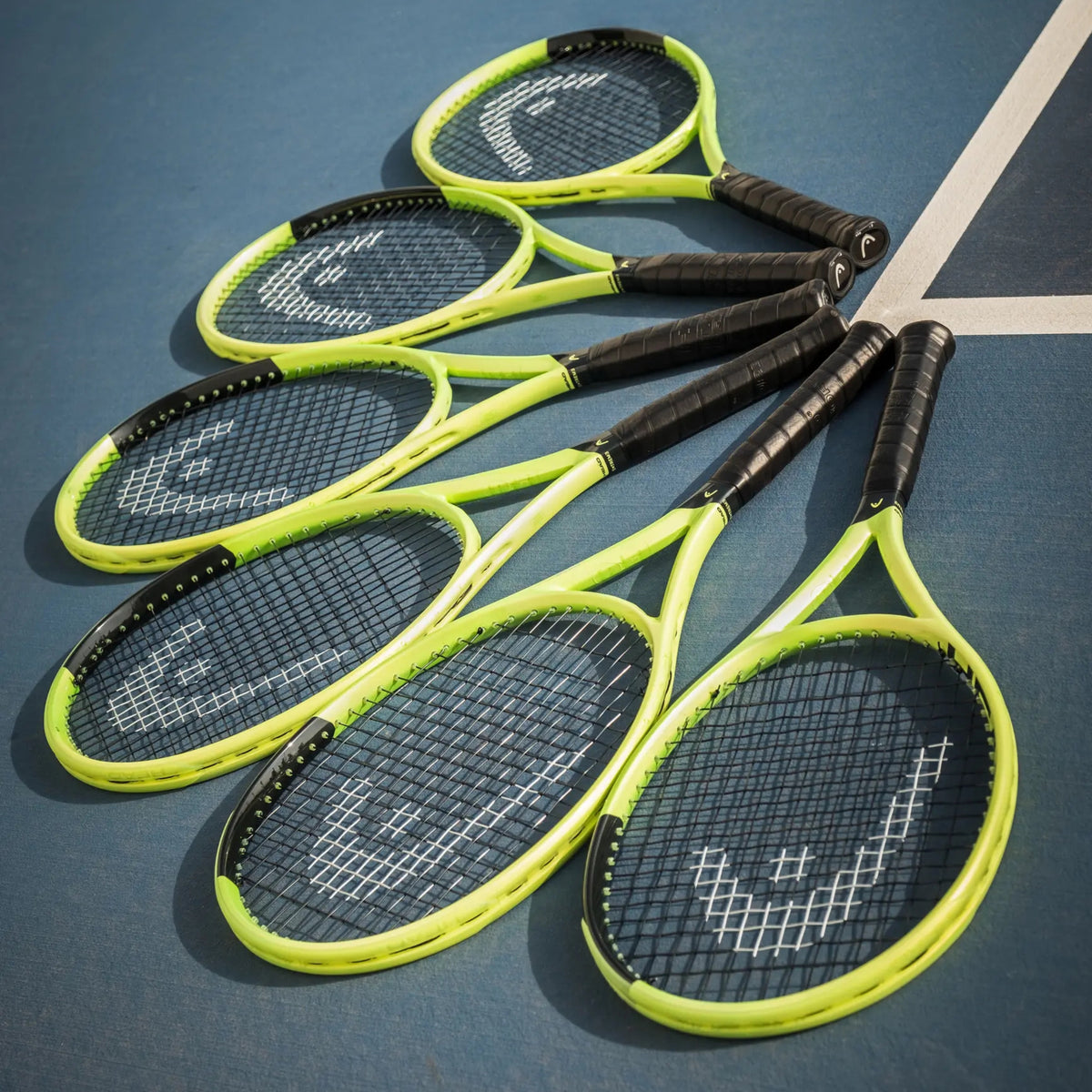 Five Head tennis rackets with bright neon yellow-green frames and black grips arranged diagonally on a blue tennis court.