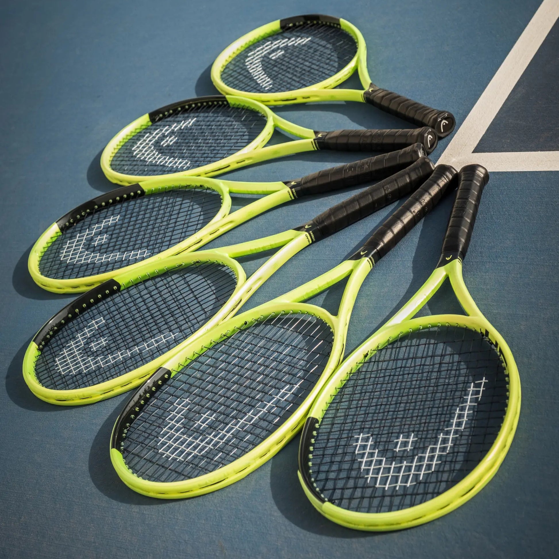 Five Head tennis rackets with bright neon yellow-green frames and black grips arranged diagonally on a blue tennis court.