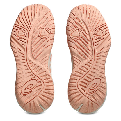 A pair of tennis shoes shown from the sole view, featuring a textured peach-pink rubber outsole with a wavy tread pattern and circular logo details on a white background.