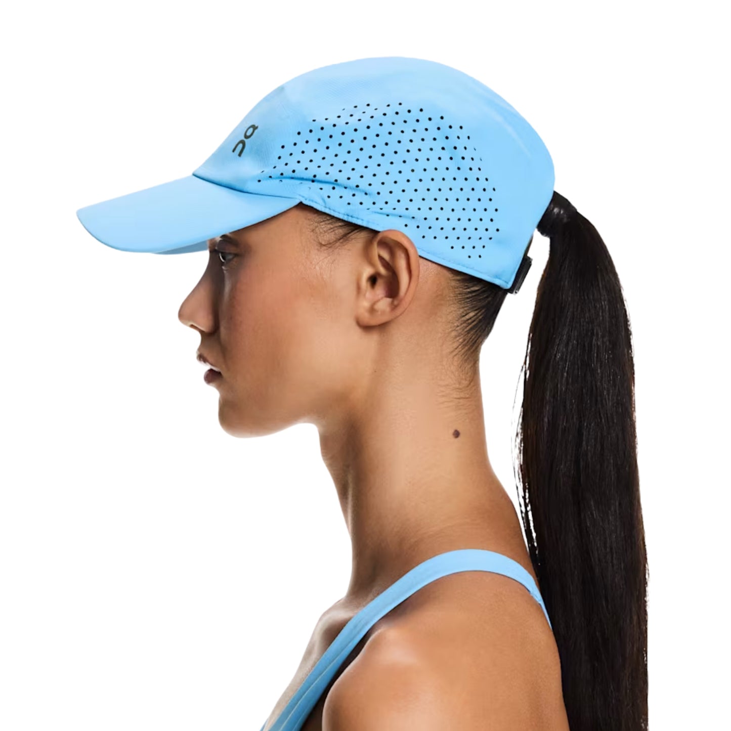 A woman in profile wearing a light blue athletic cap with a side cutout and black dotted ventilation pattern, paired with a matching light blue sports bra, against a solid white background.