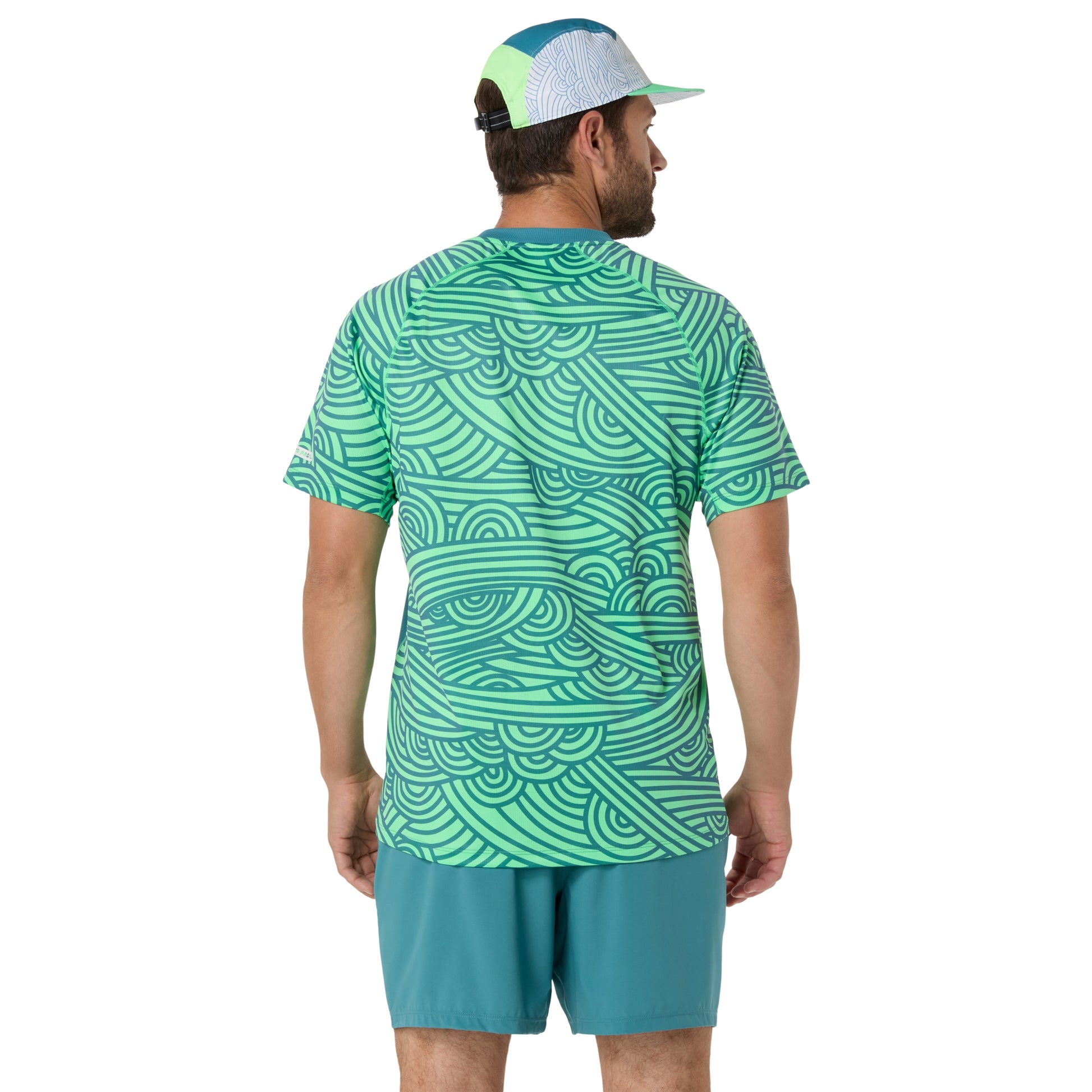 Man wearing a green patterned shirt and teal shorts on a white background