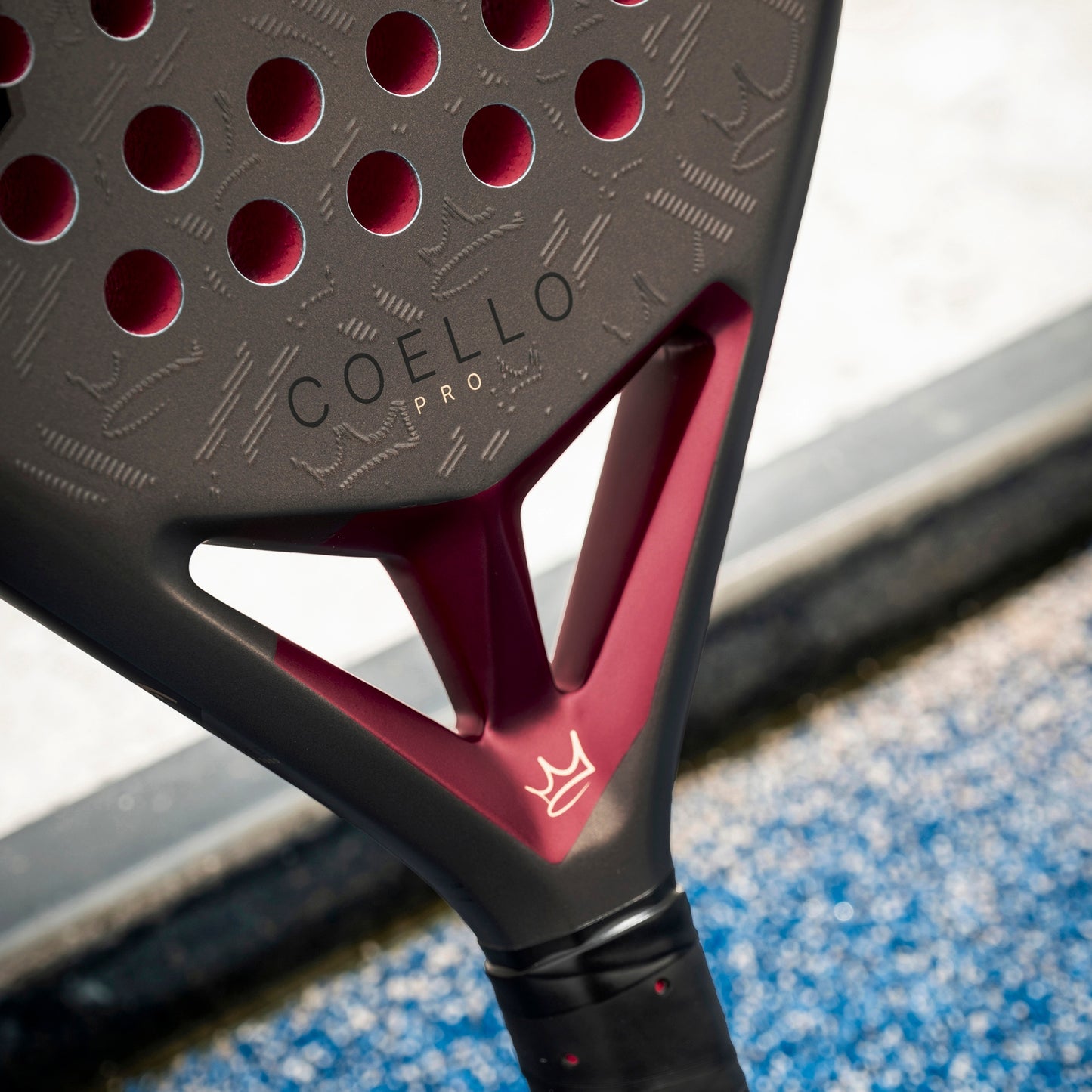 Close-up of a padel racket with 'COELLO' branding on a blurred sports court background