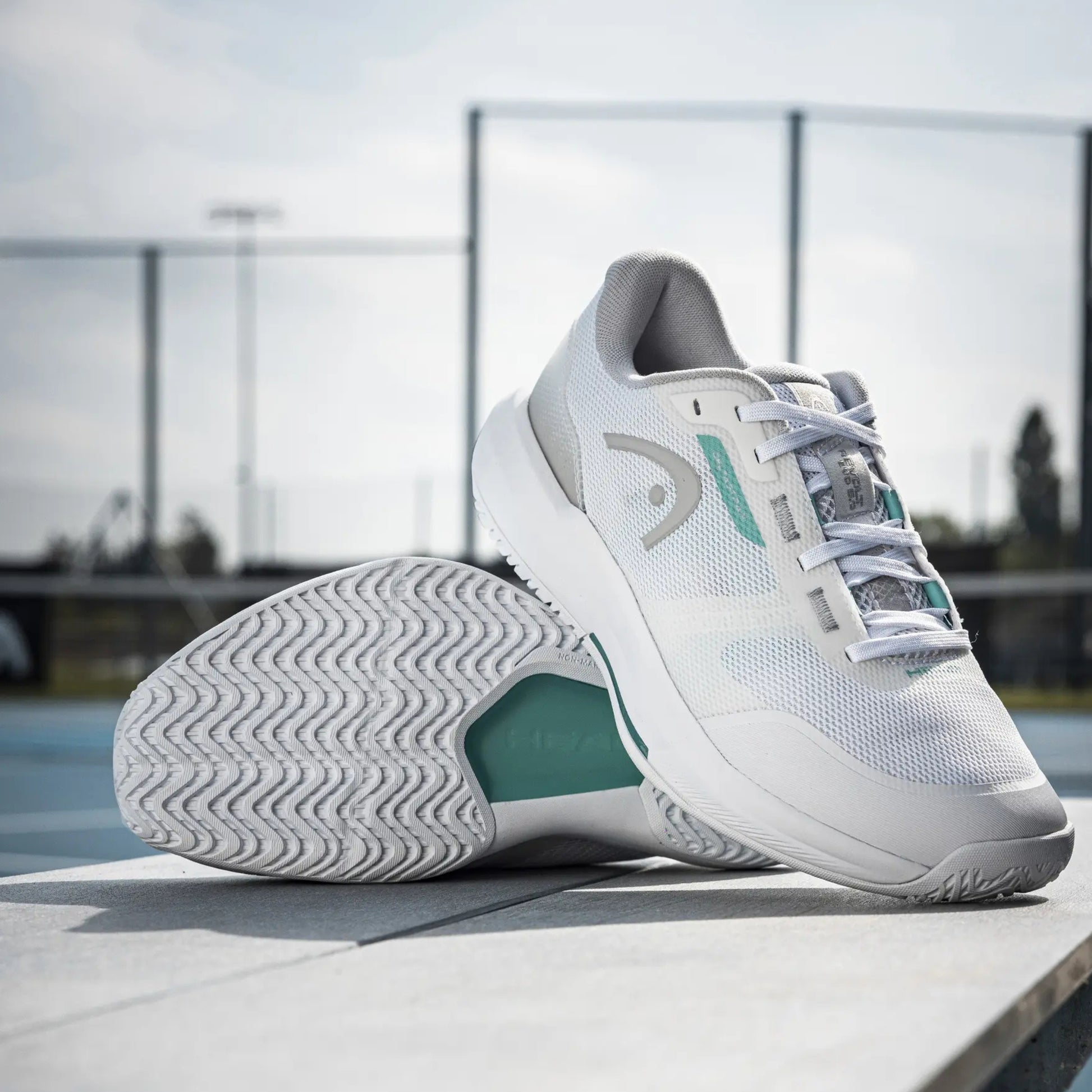 White and teal Head tennis shoes on a surface with a blurred background