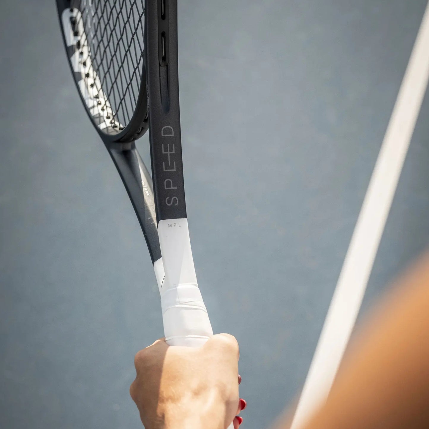 Tennis racket with 'SPEED' branding held by a person against a gray background