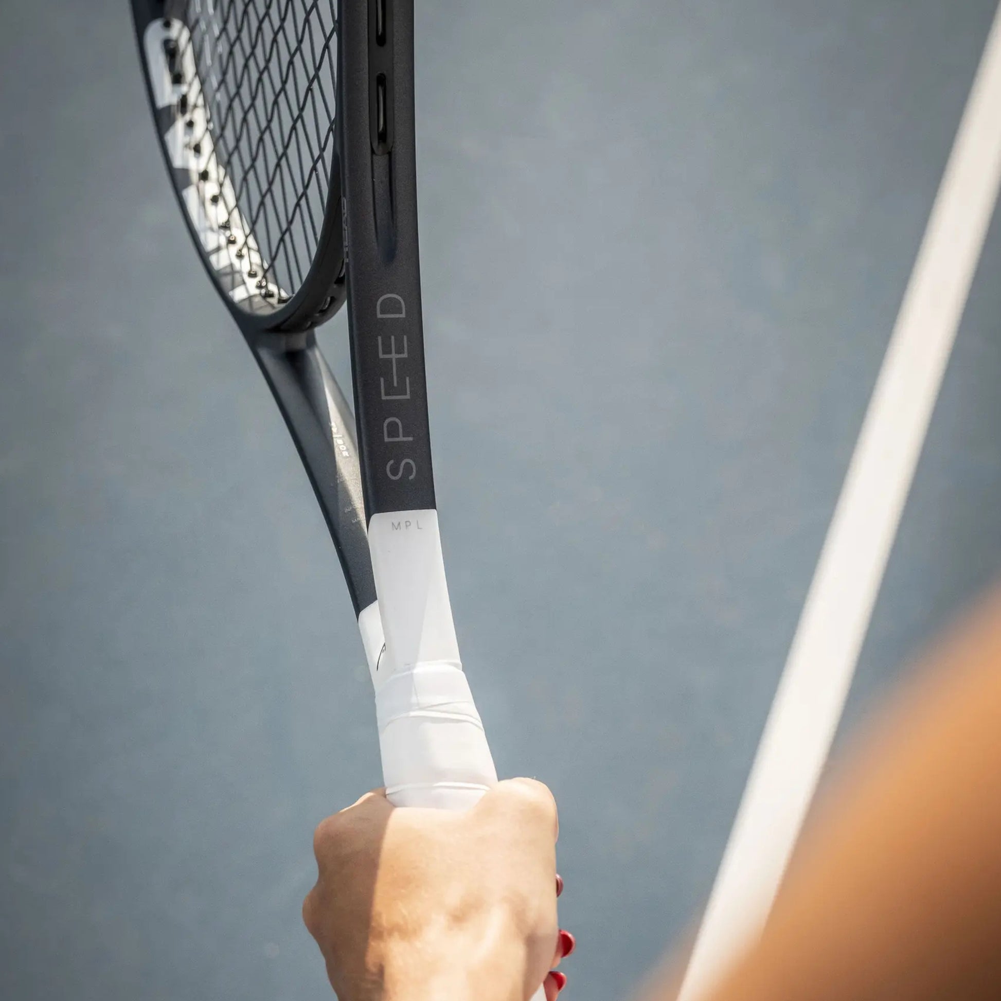 Tennis racket with 'SPEED' branding held by a person against a gray background