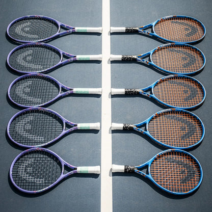 Six Head tennis rackets arranged in two vertical rows on a blue tennis court, with purple, blue, black, and orange racket frames and strings.