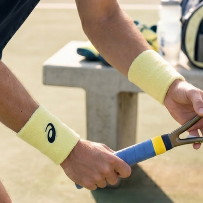 Person holding a tennis racket with yellow wristbands featuring a logo.