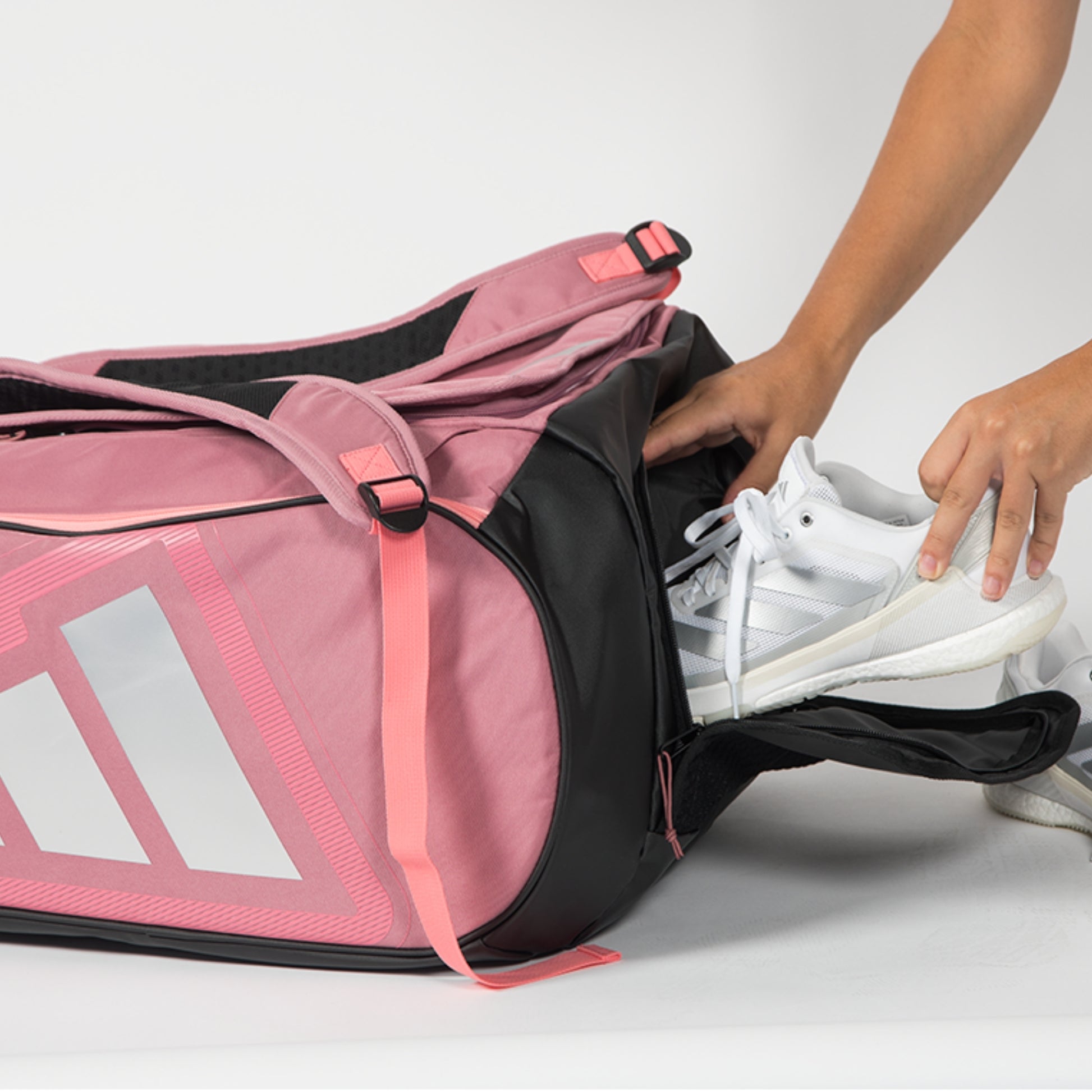 Person placing a white sneaker into a pink padel bag with Adidas logo.