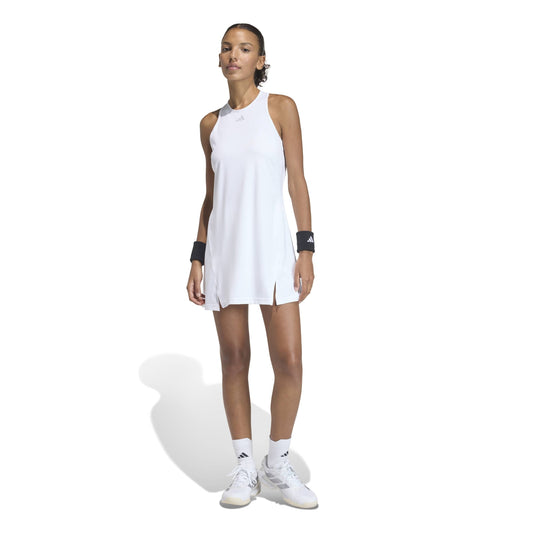 Woman wearing a white sleeveless adidas dress and white sneakers on a white background