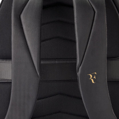 Close-up of a black backpack with a gold logo on the strap.